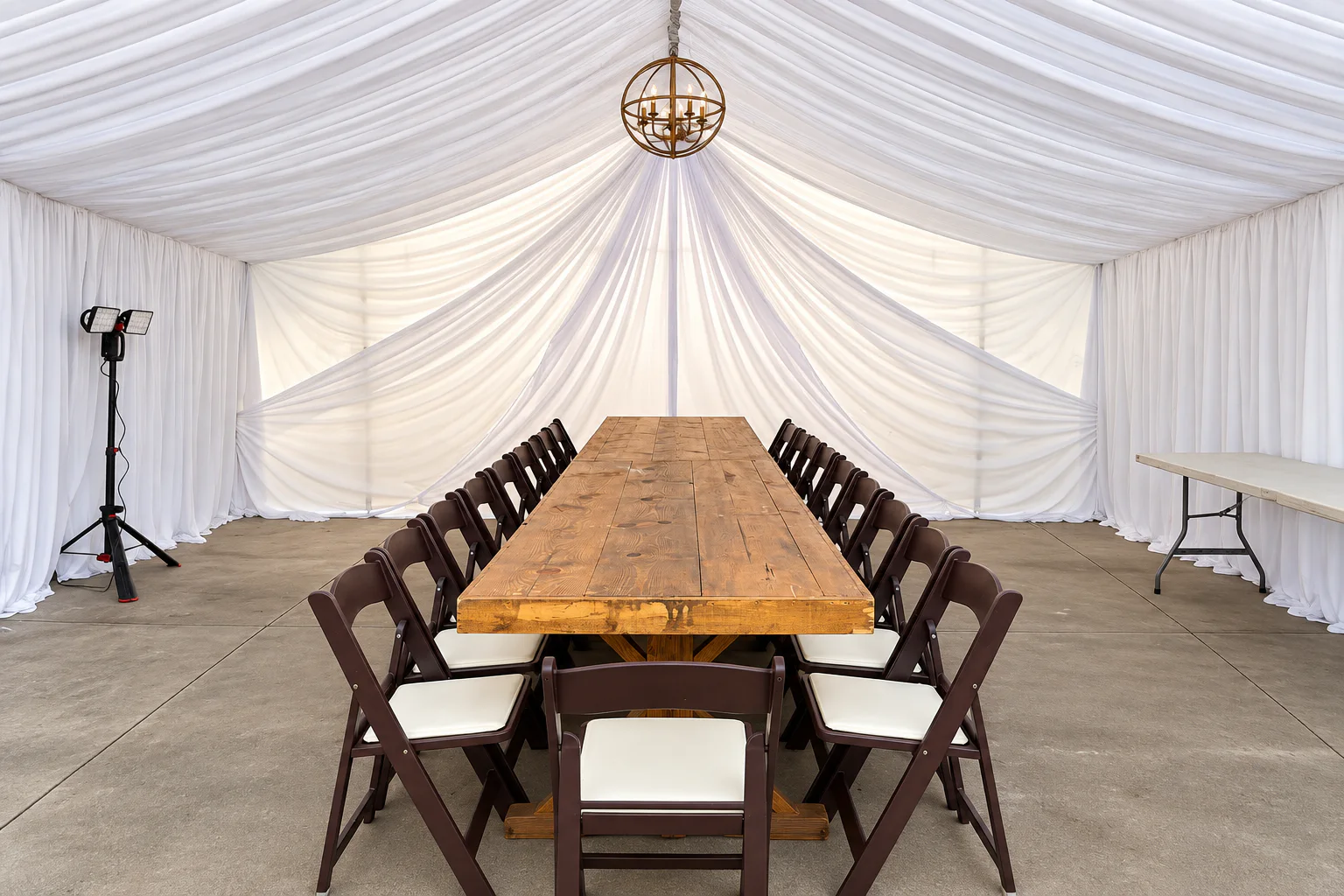 Long rustic banquet table and chairs framed by white canopy draping